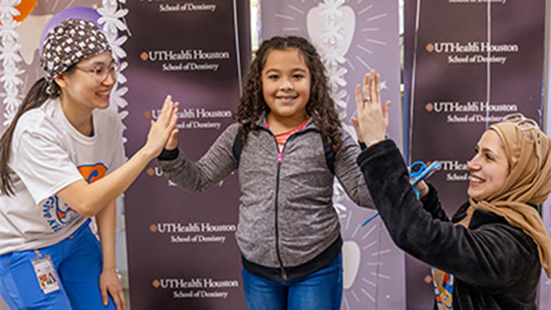 Posed image of young girl with arms raised standing between two medical students giving each a high five